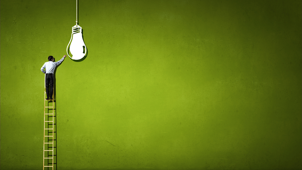 Back view of businessman standing on ladder and reaching light bulb