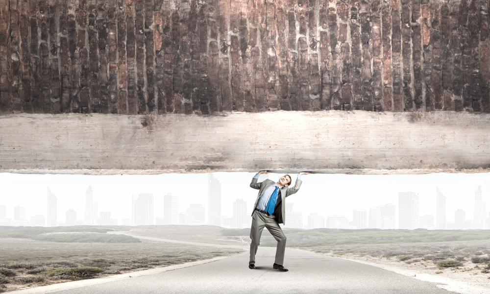 Young powerful businessman lifting brick wall above head