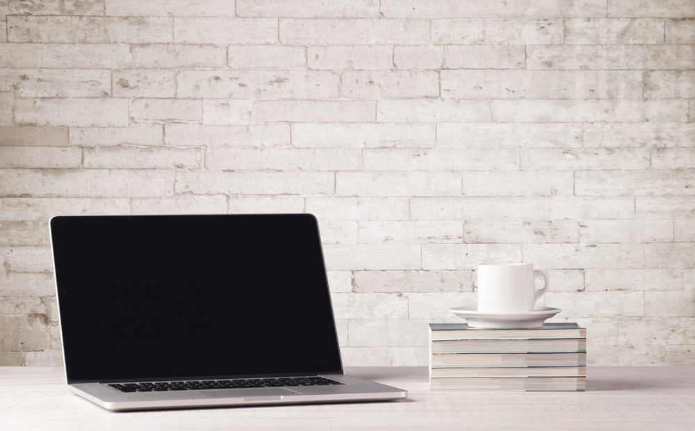 An open laptop on an office desk with flower, coffee, books in front of white brick wall background concept-1