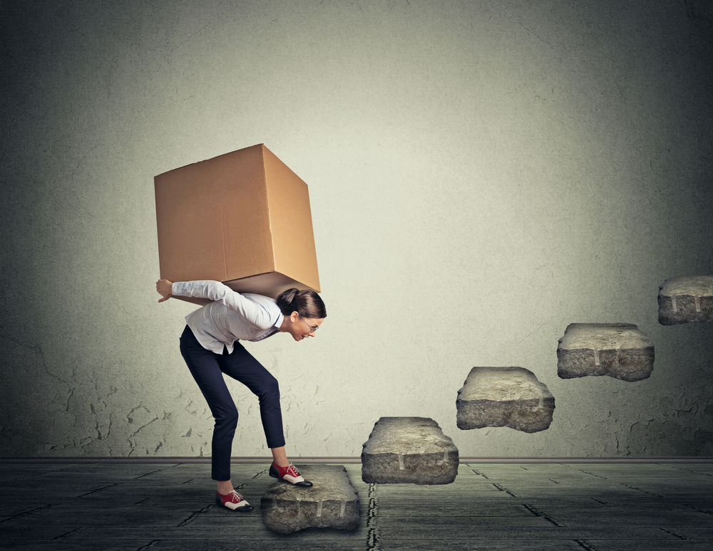 Difficult task perspective concept. Young slim woman carrying large heavy box on her back upstairs