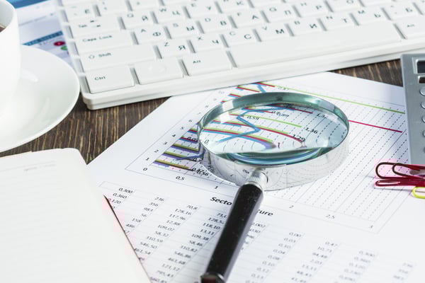 Magnifing glass and documents with analytics data lying on table-1